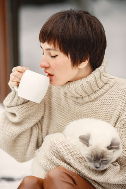 年轻穿着白毛衣和白猫一起喝茶的女人的特写肖像模型人窗户
