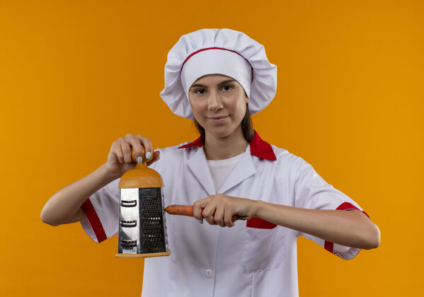 请等一下穿着厨师制服的年轻快乐的白人厨师女孩拿着烤炉和胡萝卜放在橘子上 留有复印空间女孩厨师制服