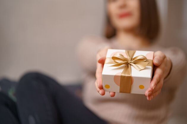 圣诞节女人手里拿着包好的白色盒子和金色的蝴蝶结 专注于盒子礼物华丽惊喜