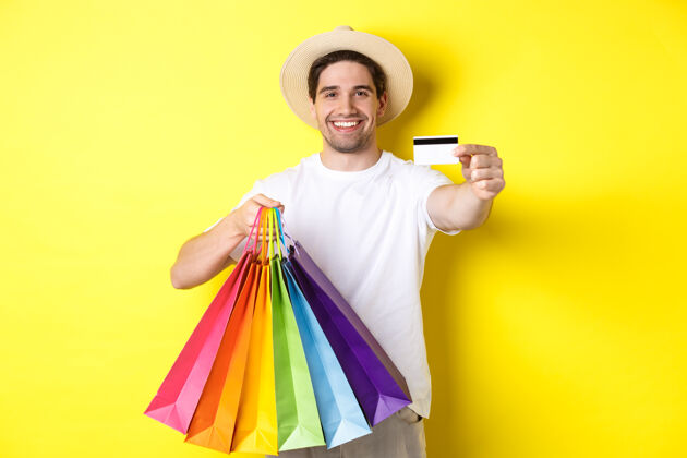 假日微笑的年轻人用信用卡买东西 拿着购物袋 看起来很开心 站在黄色的背景上表情男人模特