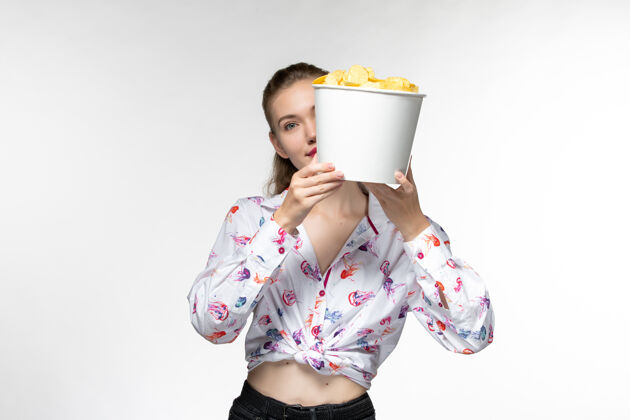 篮子正面图：年轻的女性拿着篮子 拿着薯片 在白色的表面上看电影电影院漂亮电影