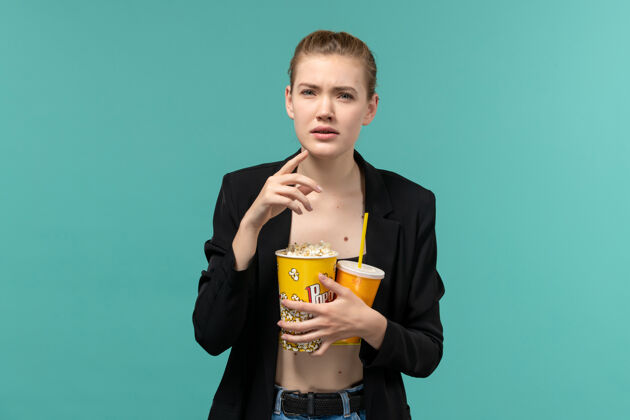 电影正面图：年轻女子拿着爆米花喝酒 在蓝色的水面上看电影抱电影剧院