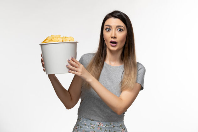 土豆正面图：白色表面上拿着薯片的年轻女性手提篮遥控篮子电影院