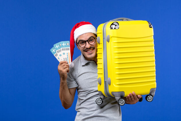 圣诞节正面图：年轻的男性拿着包和机票在一架蓝色墙壁的男性航班度假飞机上专业工程师男人