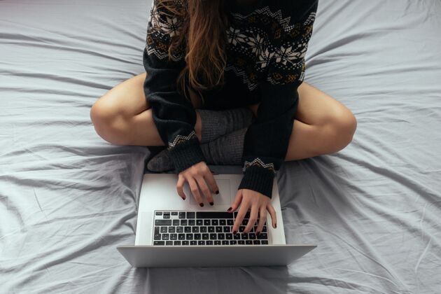 打字女性交叉着双腿坐在床上用笔记本电脑打字室内工作床