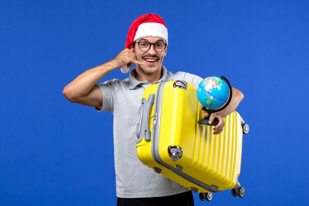 地球仪正面图年轻男性手持地球仪和黄色袋子在蓝色墙壁飞机上度假旅行游泳成人包