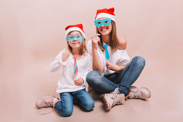 装饰快乐的妈妈和她可爱快乐的女儿戴着狂欢节面具和圣诞老人的帽子童年聚会女人