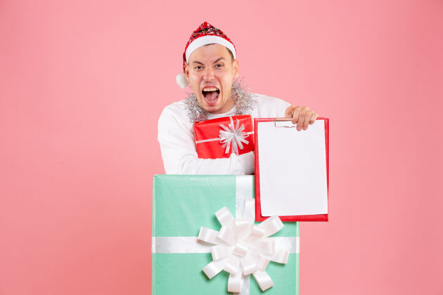 礼物正面图年轻的男性在目前持有文件 目前在粉红色的背景丝带圣诞节视图