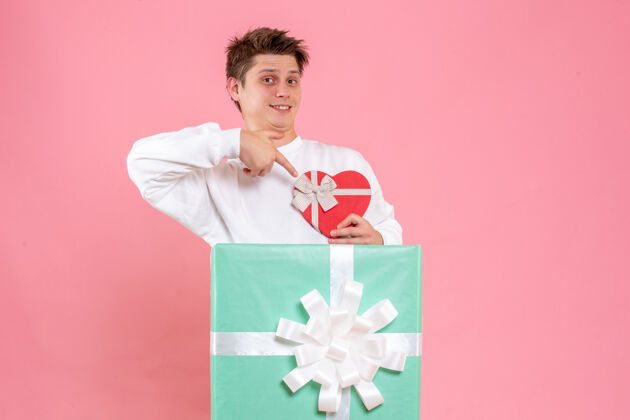 礼物正面图：年轻男性在粉色背景上赠送礼物肖像心形圣诞