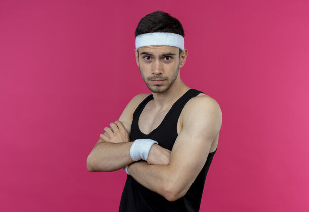 粉色戴着头带的年轻运动型男子 自信严肃的表情 双臂交叉放在胸前 粉色的上方站立长相运动