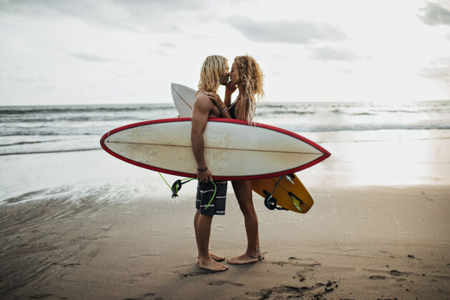 浪漫帅哥和他的女朋友在大海的背景下接吻 手里拿着冲浪板爱感情情人