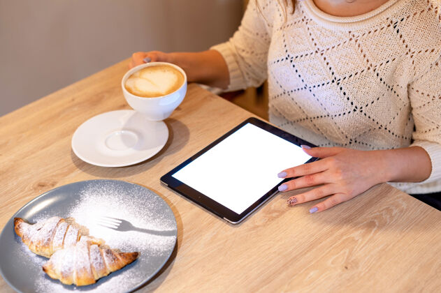 拿铁一个女人正在用平板电脑把一杯咖啡 甜点放在木桌上智能室内数码