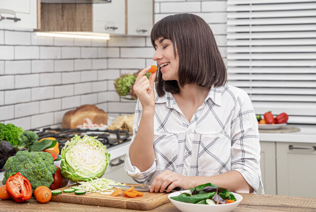 新鲜在现代厨房的背景下 漂亮的黑发女郎微笑着在沙拉上切蔬菜年轻烹饪饮食