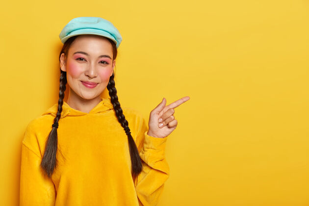 广告高兴开朗的韩国女模特站在一旁 露出冷冰冰的空白 化着妆 有两个格子 戴着帽子和黄色的运动衫天鹅绒朋友快乐