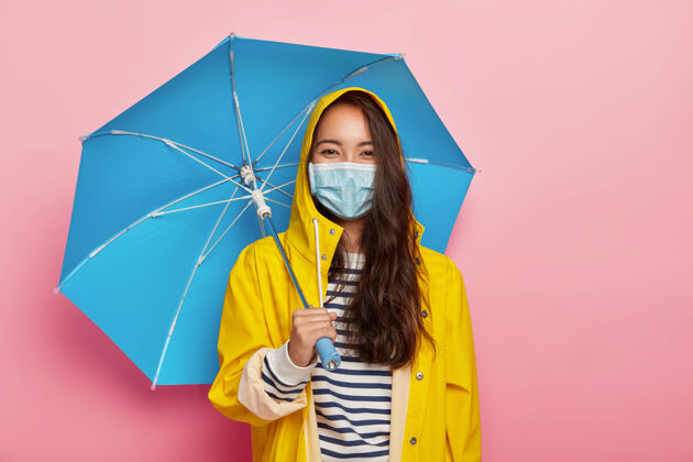穿亚洲女人戴着防护面具 在雨天面对空气污染 站在雨伞下 穿着黄色雨衣雨衣面具环境