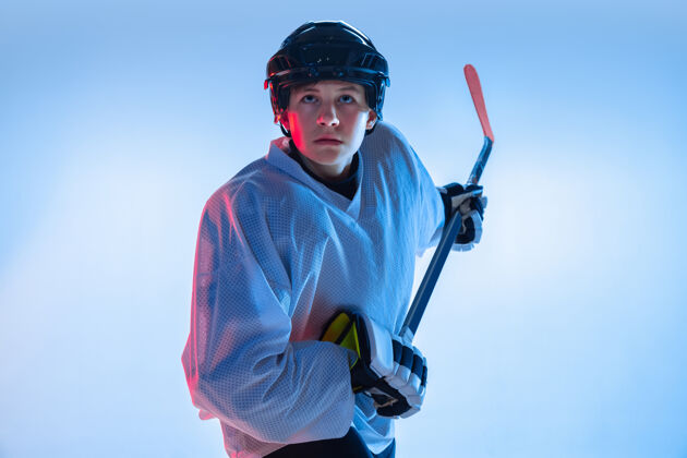 运动装年轻人年轻的男性冰球运动员 在霓虹灯下用棍子粘在白墙上运动员戴着设备和头盔练习运动的概念 健康的生活方式 运动 运动 动作棒男孩活跃