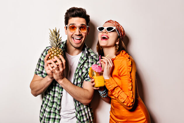 白色t恤穿着橙色裙子的漂亮女孩和穿着绿色衬衫 戴着墨镜的男人在笑 摆着菠萝和鸡尾酒的姿势情侣菠萝头带