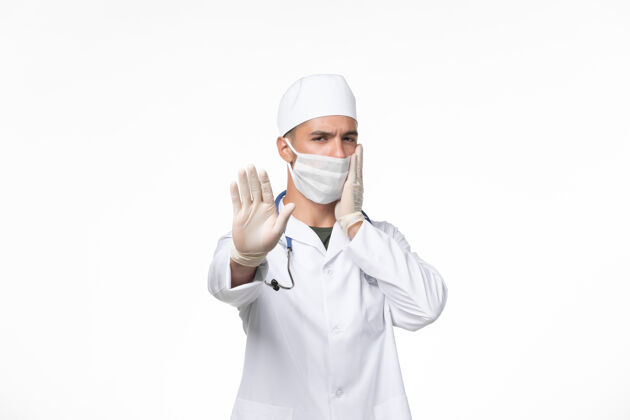 医学正面图：男医生穿着医疗服 戴着防毒面具 在淡白色的墙壁上传播病毒人视图专业
