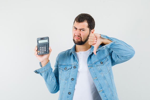 年轻复古风格的男人拿着计算器 在夹克衫 t恤衫上竖起大拇指 看起来很不满意正视图思考成人男人