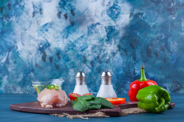 生的鸡胸肉和蔬菜放在切菜板上 而不是放在蓝色表面的粗麻布餐巾上鸡配料鸟