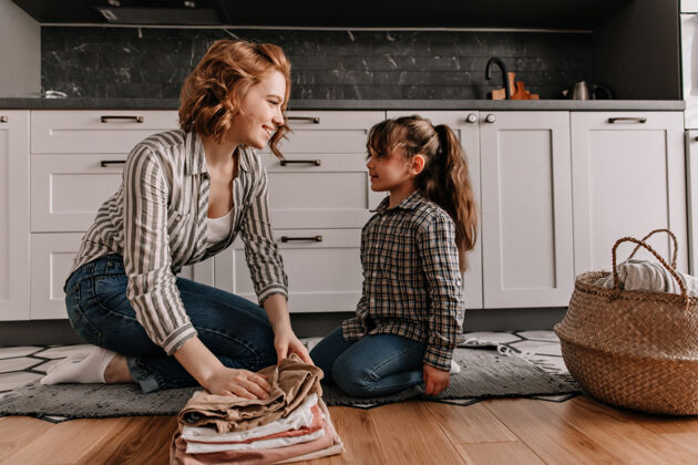 肖像妈妈和女儿穿着相似的衣服 坐在厨房的地板上 叠着洗好的衣服 谈笑风生父母妈妈公寓