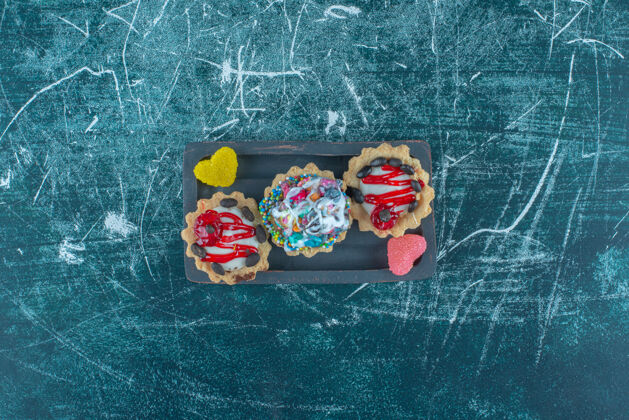 顶部蓝色背景的盘子上放着一小包纸杯蛋糕和果酱高质量的照片美味草莓糖