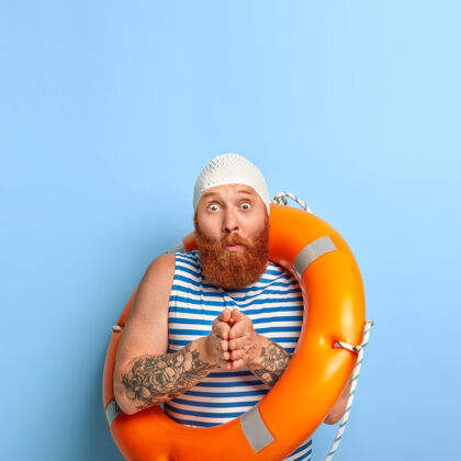 条纹垂直拍摄的是一个惊讶的红发男人 他留着浓密的胡须 双手紧握在一起 准备潜水 穿着保护性橡胶泳衣 水手背心 眼睛露了出来游泳帽子胡须
