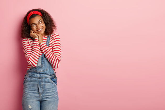 粉色快乐的千禧一代美国黑人女孩高兴地看着旁边 戴着红色头带 条纹套头衫和牛仔工作服装束牛仔女性