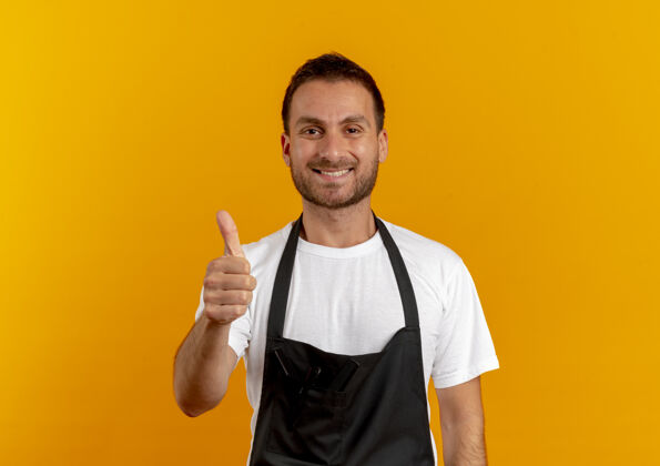男人穿着围裙的理发师站在橘色的墙上 面带微笑 高兴地竖起大拇指 望着前面微笑市民T恤