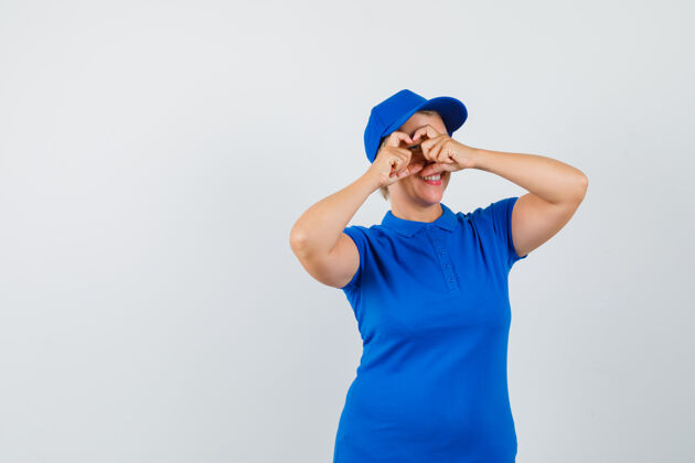 女士成熟的女人穿着蓝色t恤展示心形 看起来很高兴女性活跃帽子