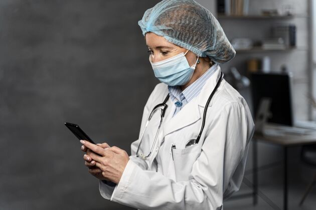 职业侧视图的女医生与医疗面具和发网举行智能手机工作职业发网