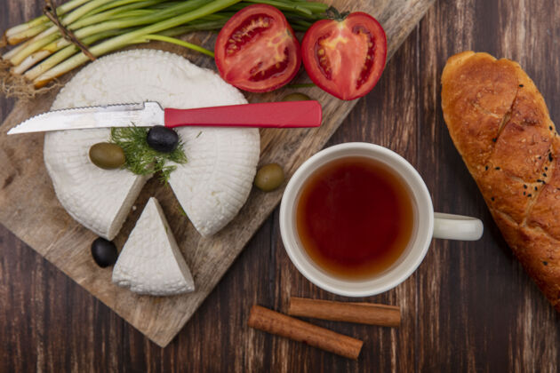 面包俯视图：一个架子上放着一杯茶和一条面包 架子上放着西红柿 橄榄和葱木头羊奶餐