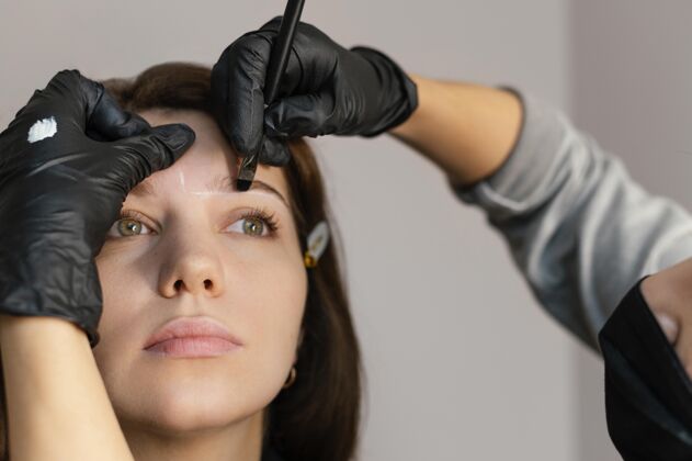 女人从美容师那里得到眉毛治疗的女人的正视图美容师面膜临床医生