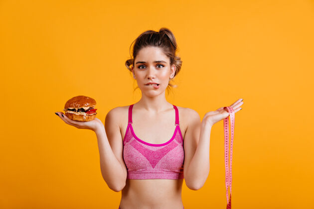 不健康拿着芝士汉堡的犹豫不决的女人健身面子饮食