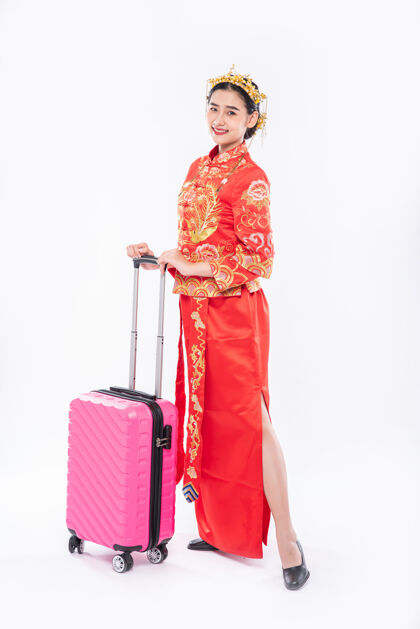 手提箱穿旗袍套装的女士在中国新年旅行时使用粉色旅行包文化传统服装中国文化