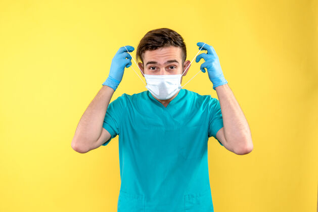 前面黄色墙上戴着手套和面罩的男医生的正面图人人外科手术