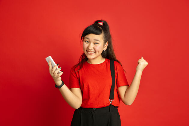 金融在红色工作室背景上孤立的亚洲青少年的肖像休闲风格的美丽的深褐色女性模特人类情感的概念 面部表情 销售 广告快乐 手持智能手机职业工作人类