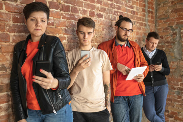 沙发一群快乐的白人年轻人站在砖墙后面分享来自智能手机或平板电脑的新闻 照片或视频 玩游戏 享受乐趣社交媒体 现代科技技术表演平板电脑