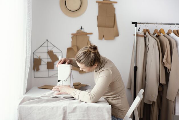 女工女裁缝手拿缝纫机在工作室工作的侧视图女装服装针线