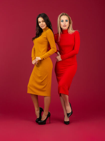 肖像两位穿着黄色和红色秋冬时尚针织连衣裙的迷人时尚女性在红墙上孤立地摆着姿势黑发秋天时尚