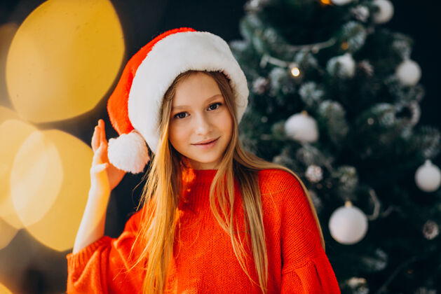 欢乐可爱的少女戴着圣诞树旁的红色圣诞帽可爱礼物礼物