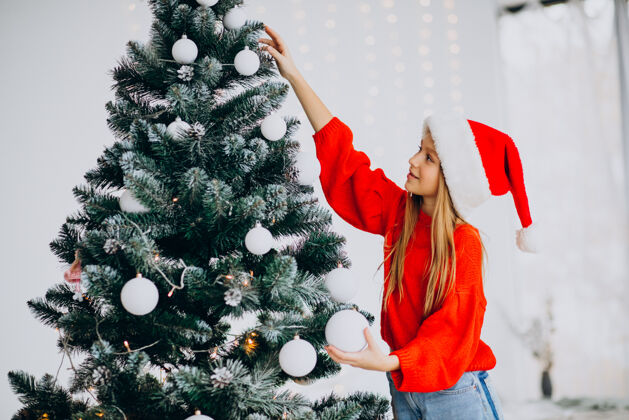 圣诞可爱的少女戴着圣诞树旁的红色圣诞帽传统圣诞老人欢呼