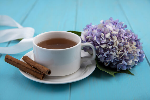 丝带茶杯和肉桂茶托的侧视图 蓝色背景上有花朵和丝带茶桌子杯子