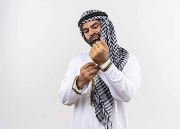 男人身着传统服装的阿拉伯男子站在白墙上 自信地修着袖扣传统修复阿拉伯语