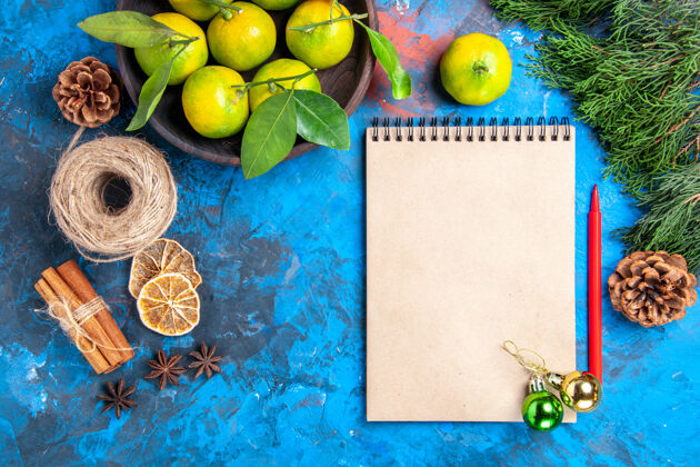 装饰品顶视图黄色橘子与树叶在木制的碗记事本红色铅笔圣诞饰品肉桂棒八角在蓝色的表面柑橘树叶奶奶史密斯