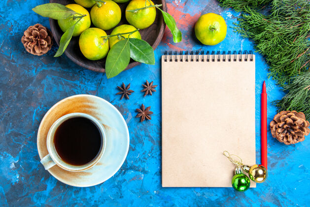 视图顶视图黄色的橘子与树叶在木制的碗记事本红色的铅笔圣诞节装饰一杯茶八角在蓝色的表面碗柑橘苹果