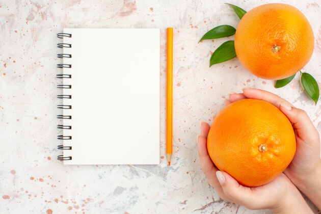 光明顶视图新鲜橘子笔记本橘子铅笔女性手上明亮的孤立表面多汁顶部柑橘
