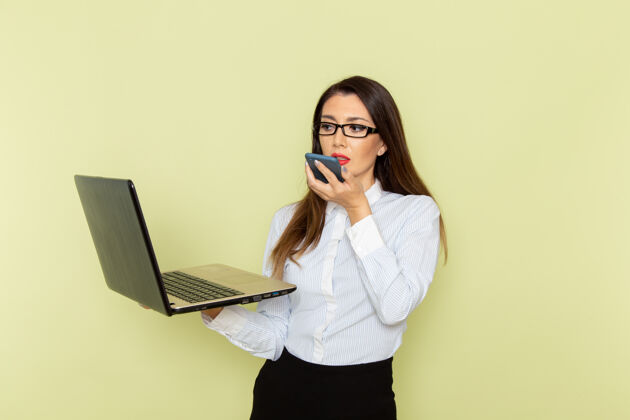 办公室身穿白衬衫和黑裙子的女上班族在绿色墙壁上手持和使用笔记本电脑通话的正面图谈话笔记本电脑裙子