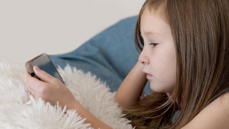 青年女孩在床上使用智能手机的侧视图设备娱乐科技