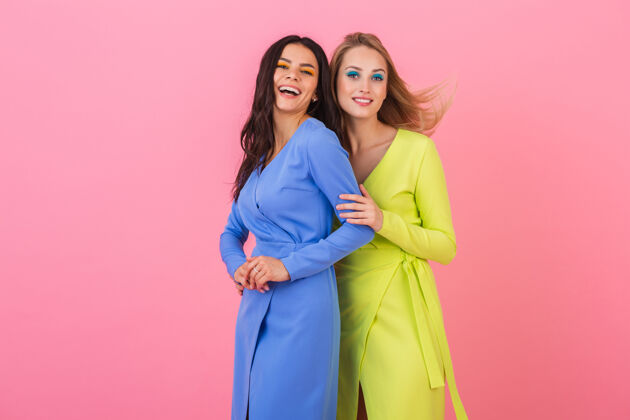 颜色两个时尚的微笑迷人的女人在粉红色的墙上摆着有趣的姿势 穿着蓝色和黄色的时髦多彩的裙子 春天的流行趋势衣服女士人